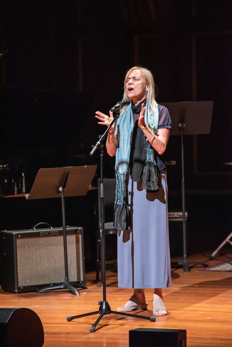 Dominique Eade closes her eyes and sings into a microphone in an unaccompanied solo performance in Jordan Hall.
