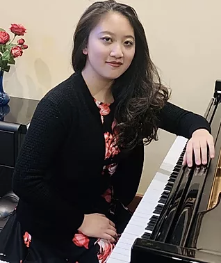 Edwina Sun smiles and rests her arm on her piano