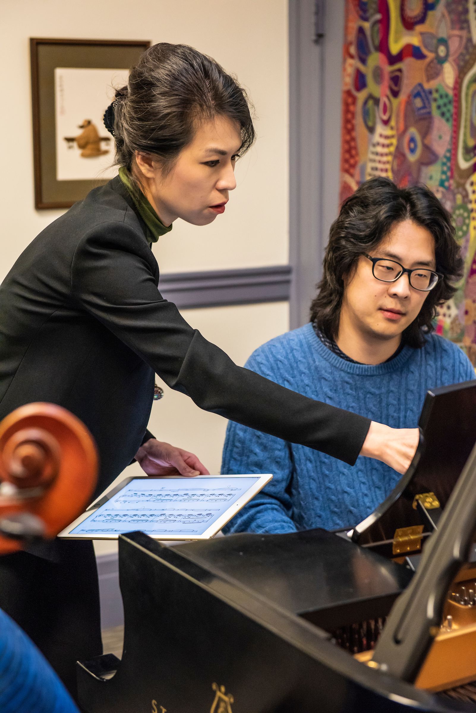 Pei-Shan Lee points toward the music for a pianist. The scroll of a cello can be seen in the foreground.
