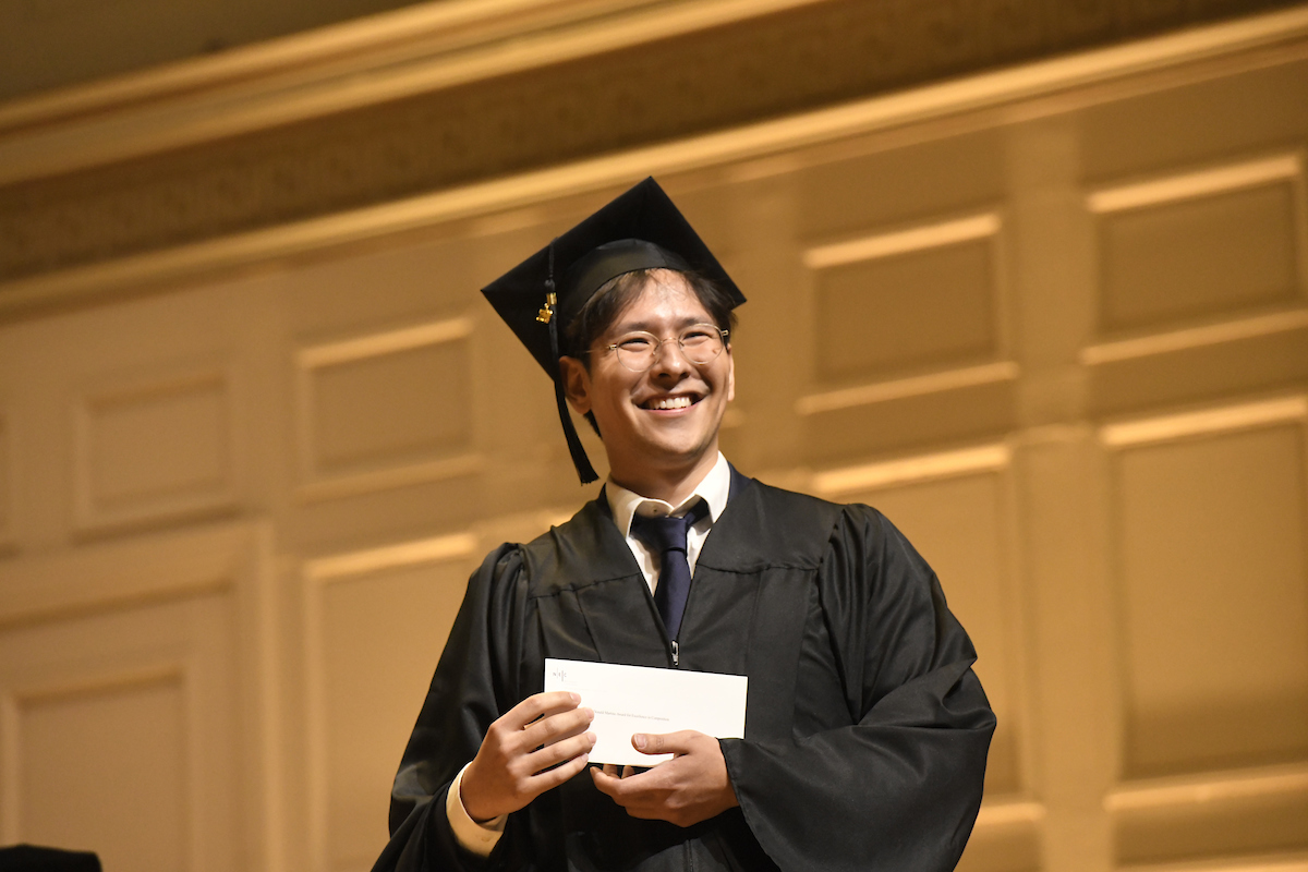 Andrew Minoo Dixon smiles with cap and gown and award
