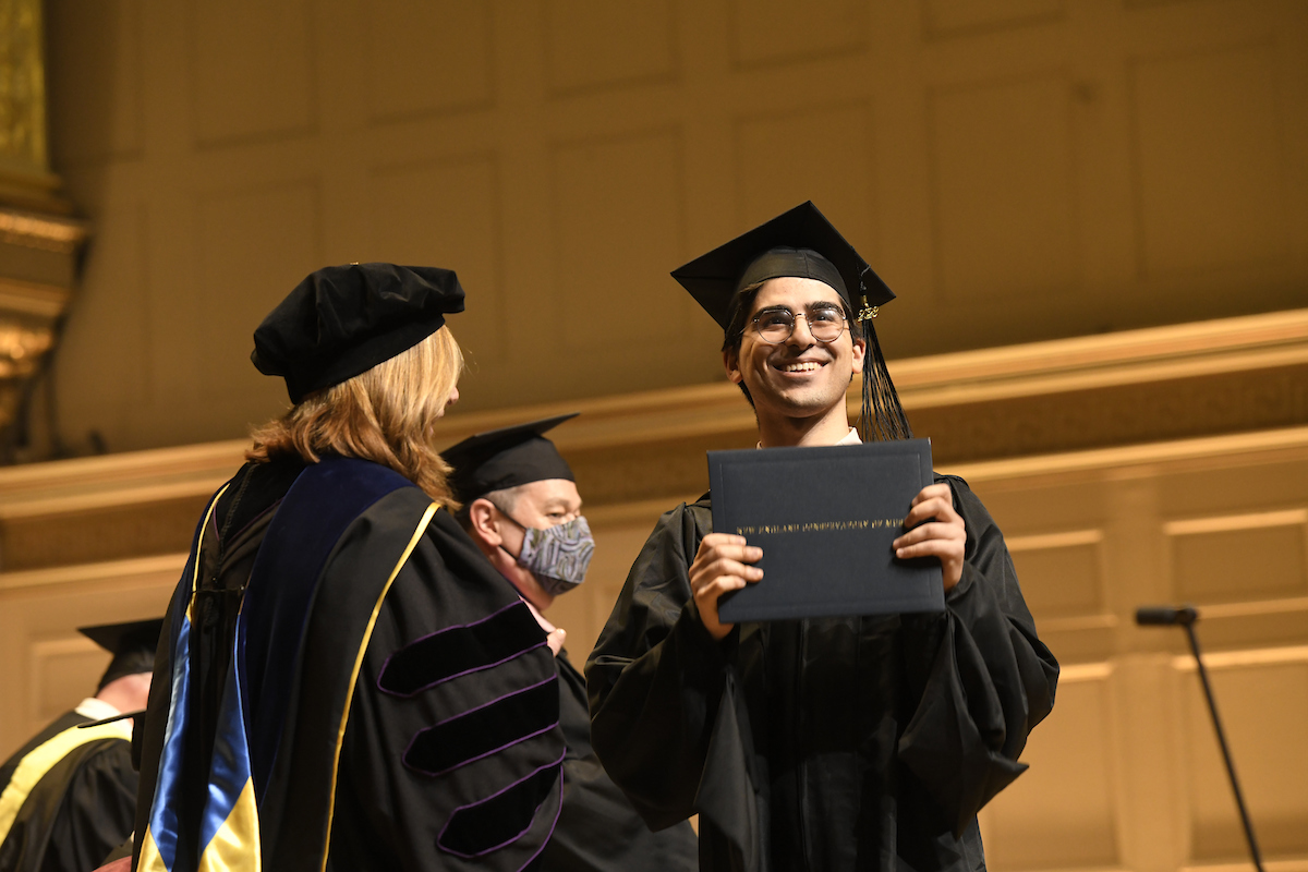 A graduate smiles with degree in hand while President Andrea Kalyn looks on
