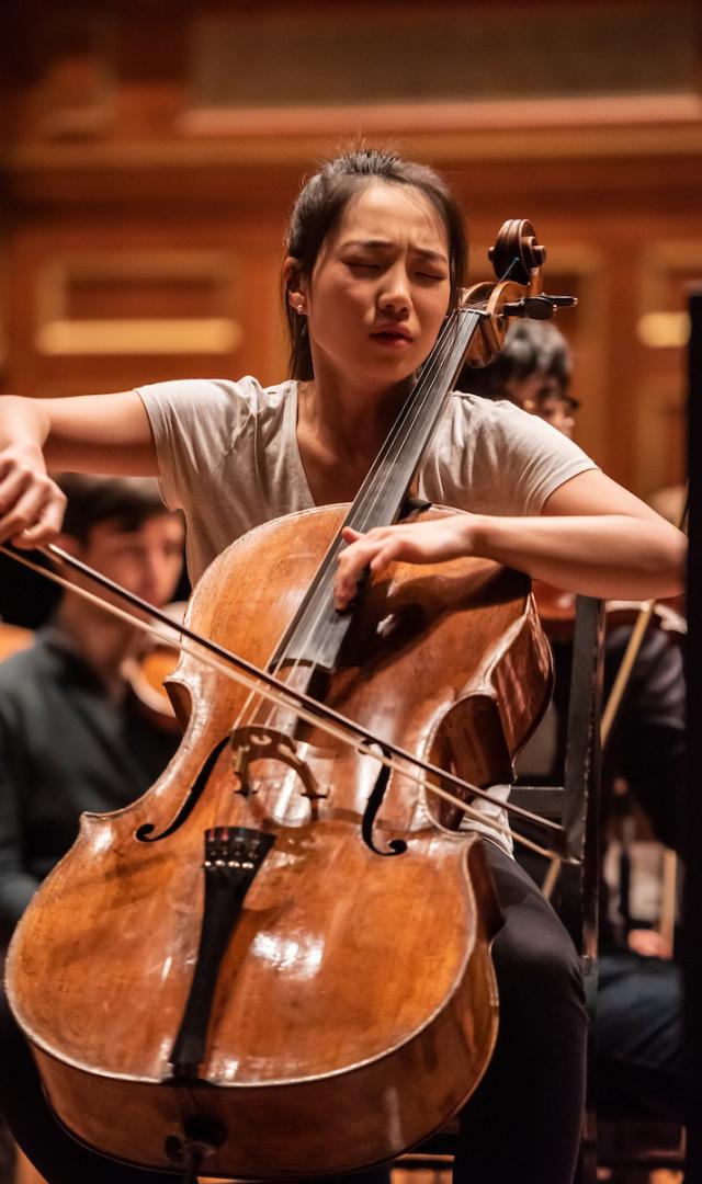 Claire Deokyong Kim plays the cello with an expression of emotion on her face.
