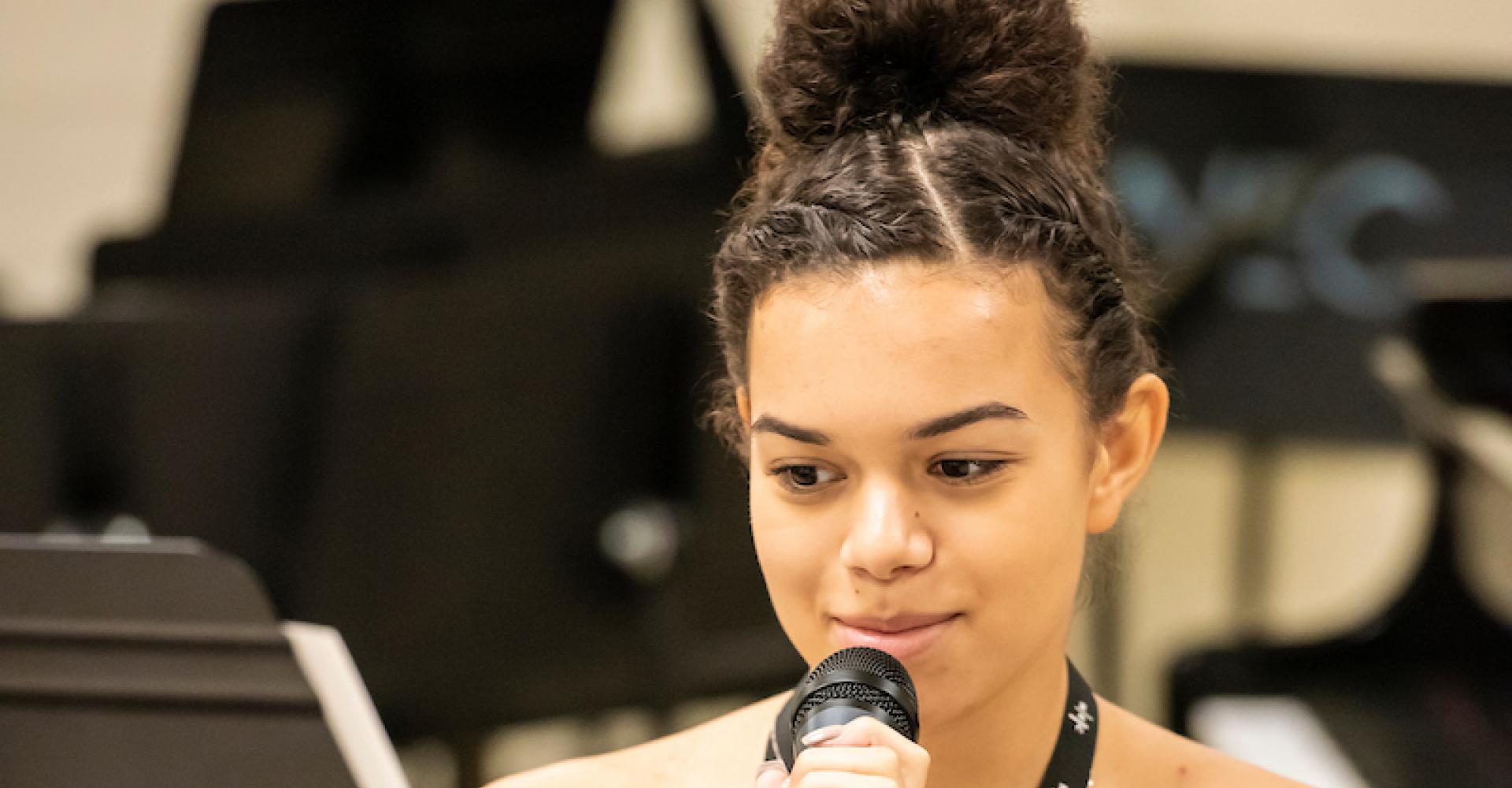 A teen jazz singer smiles and sings into a microphone at Jazz Lab.