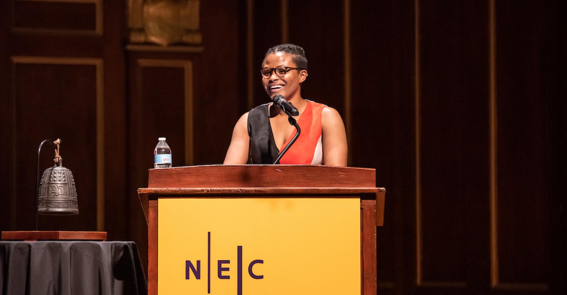 Robyn Smith delivers remarks at an NEC podium in Jordan Hall.