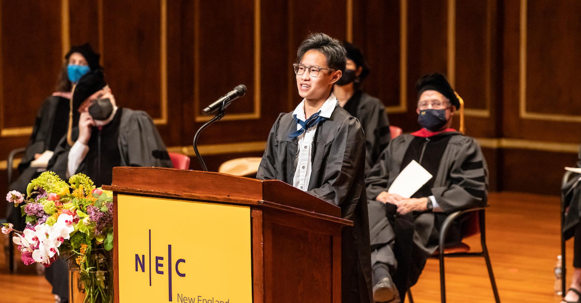 Robbie Bui speaks at a lectern from the Jordan Hall stage during Commencement 2021.