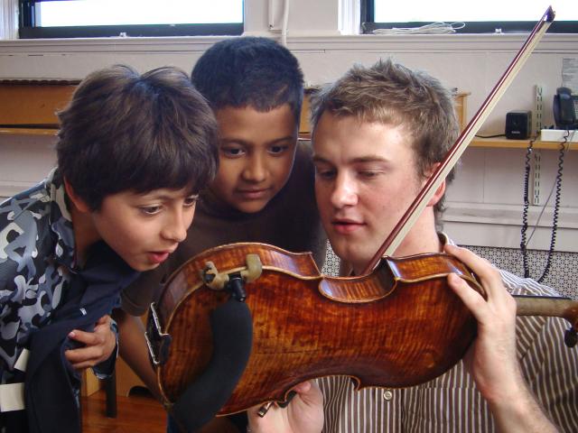A violinist show his instrument to two interested kids