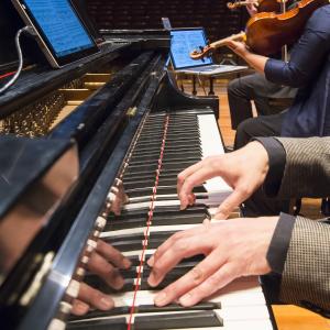 Hands on a piano keyboard with string players in background