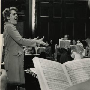 Lorna Cooke deVaron conducts while smiling and making a gesture of passion and joy.