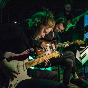 Two guitarists play with eyes closed, with dark green lighting, on Jordan Hall stage.